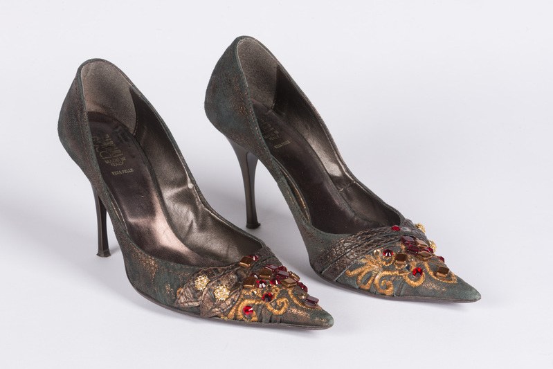 Grüne High Heels mit goldenen und roten Kristallen auf einem weißen Hintergrund, mit spitzer Zehe und Stiletto-Absatz.