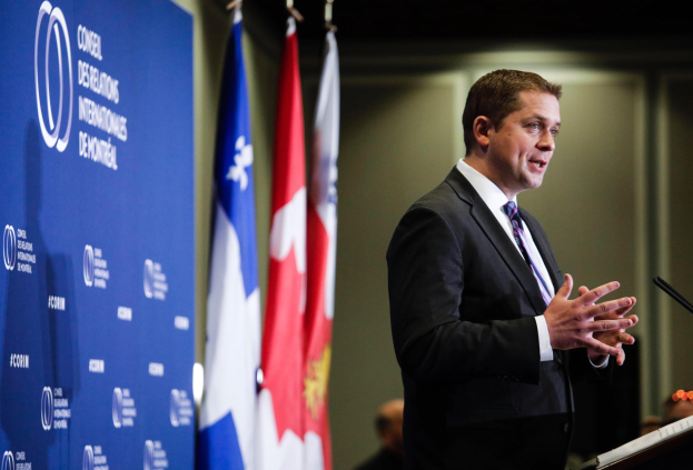 Kanadischer Premierminister am Rednerpult mit Mikrofon, Rede vor Flaggen und Banner mit Text.