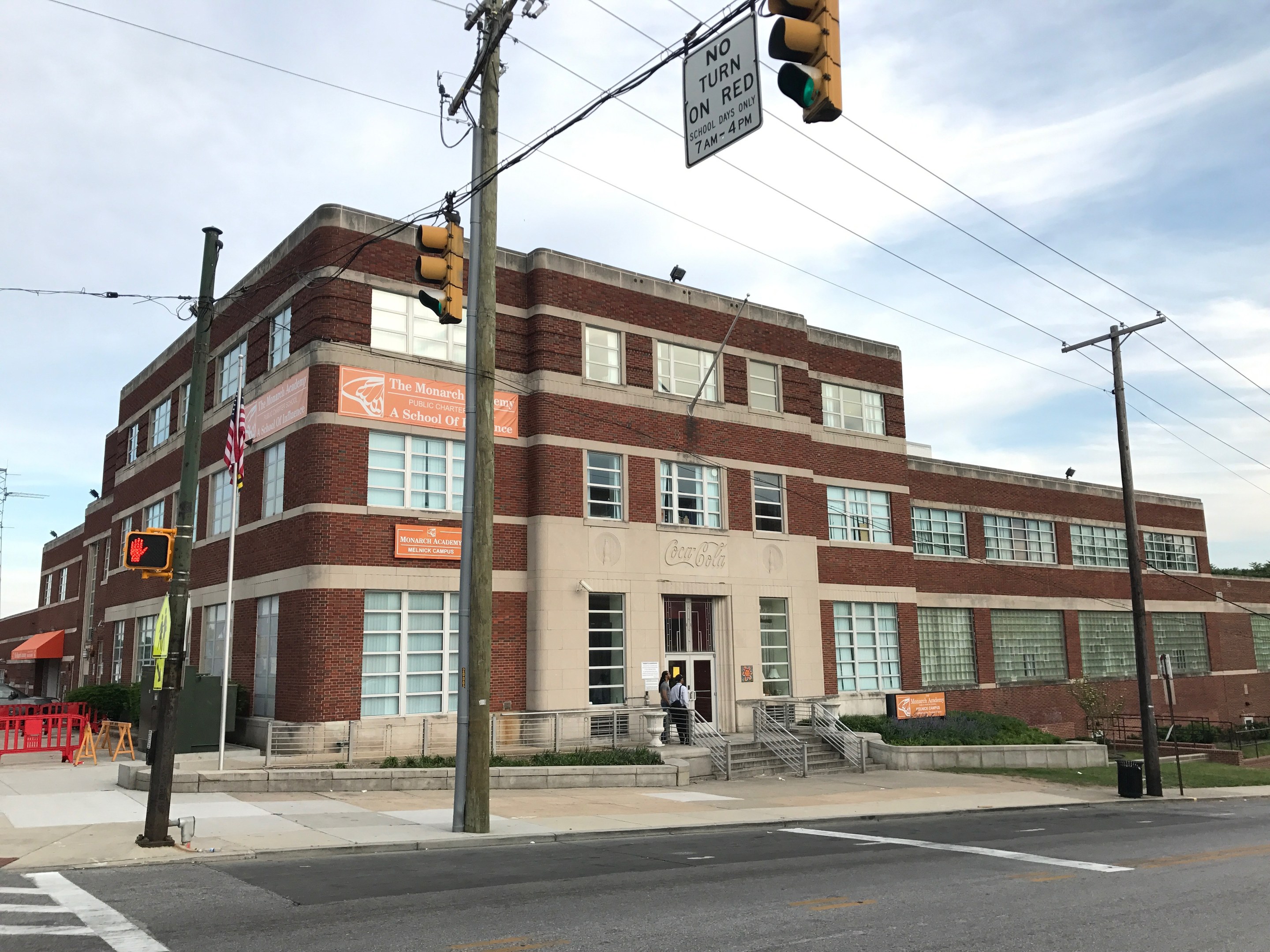 Großes Backsteingebäude mit der Aufschrift "Monarchs A-School" an einer Straßenecke mit Treppe, Geländern, Schildern und städtischen Elementen.