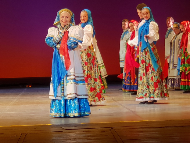 Eine Gruppe von Menschen in leuchtend bunten, detaillierten traditionellen ukrainischen Kostümen lächelt und steht fröhlich auf einer Bühne.