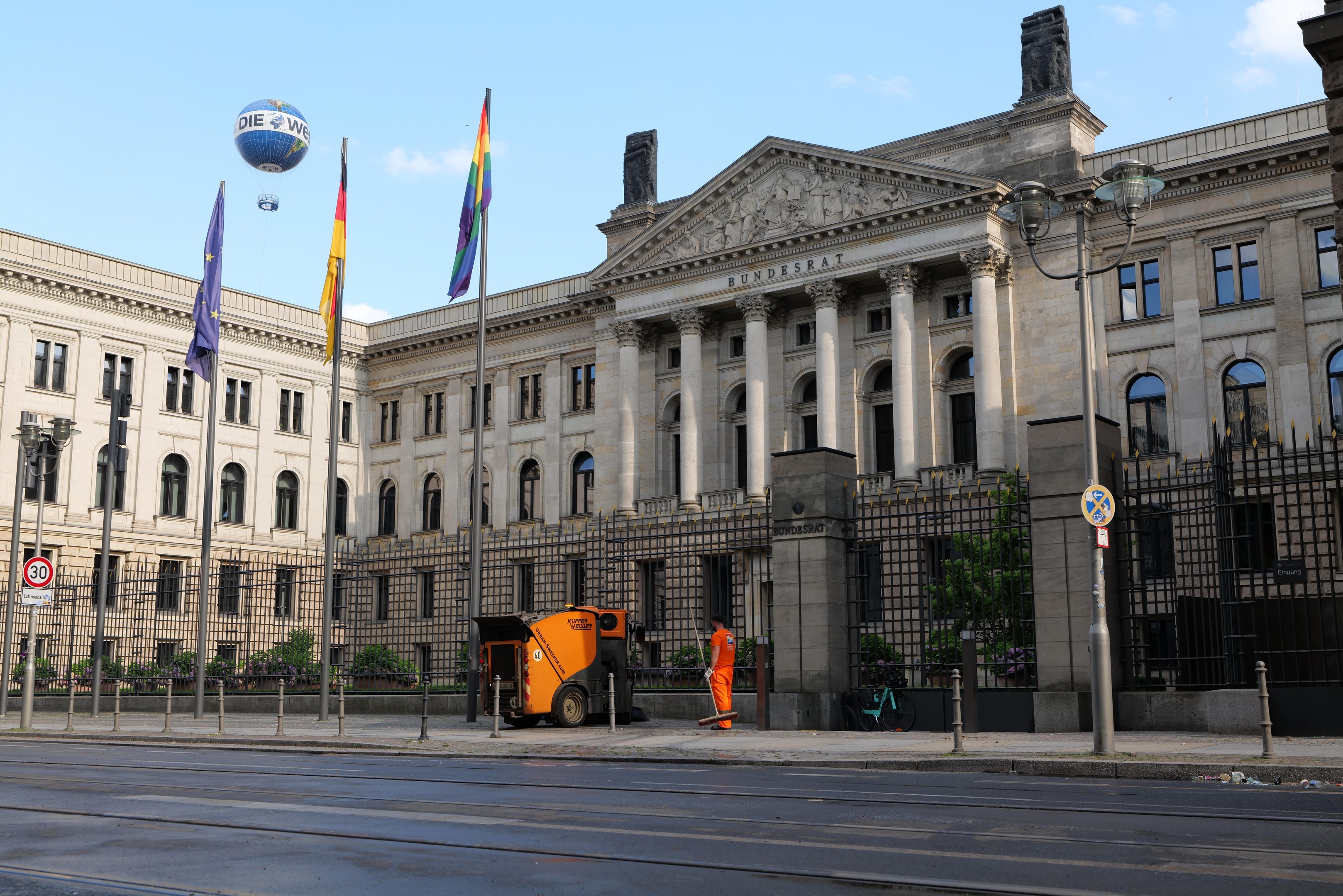 Großes modernes Gebäude mit vielen Fenstern, als Bundestag in Berlin, Deutschland identifiziert, umgeben von Straßeninfrastruktur, Fußgängern, Fahrzeugen und Bäumen unter einem bewölkten Himmel.