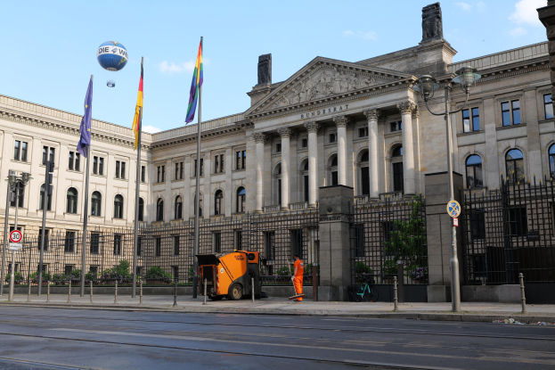 Großes modernes Gebäude mit vielen Fenstern, als Bundestag in Berlin, Deutschland identifiziert, umgeben von Straßeninfrastruktur, Fußgängern, Fahrzeugen und Bäumen unter einem bewölkten Himmel.