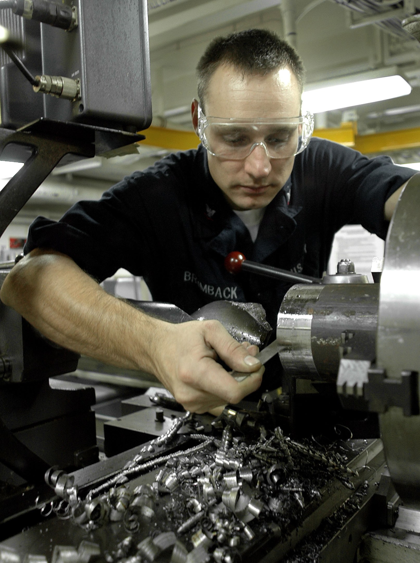 Ein Fräser mit Brille bedient eine Maschine in einer gut beleuchteten Fabrikumgebung.
