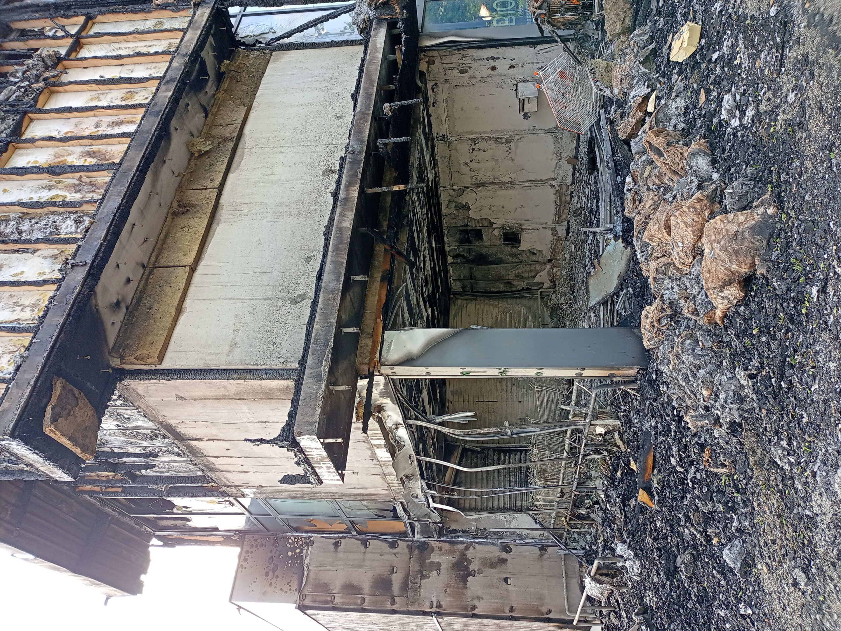 Verkohlte Überreste eines durch Feuer beschädigten Gebäudes mit Schutt auf dem Boden, vor einem Himmelhintergrund.