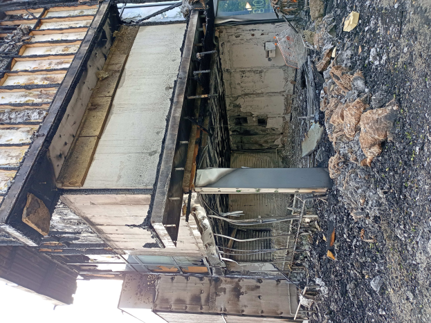 Verkohlte Überreste eines durch Feuer beschädigten Gebäudes mit Schutt auf dem Boden, vor einem Himmelhintergrund.