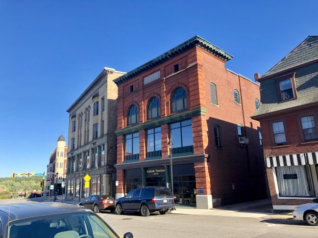 Stadtstraße in einem historischen Viertel mit parkenden Autos, mehrstöckigen Gebäuden mit Fenstern, Laternen, Schildern, Verkehrszeichen, Bäumen und einem sichtbaren Himmel.