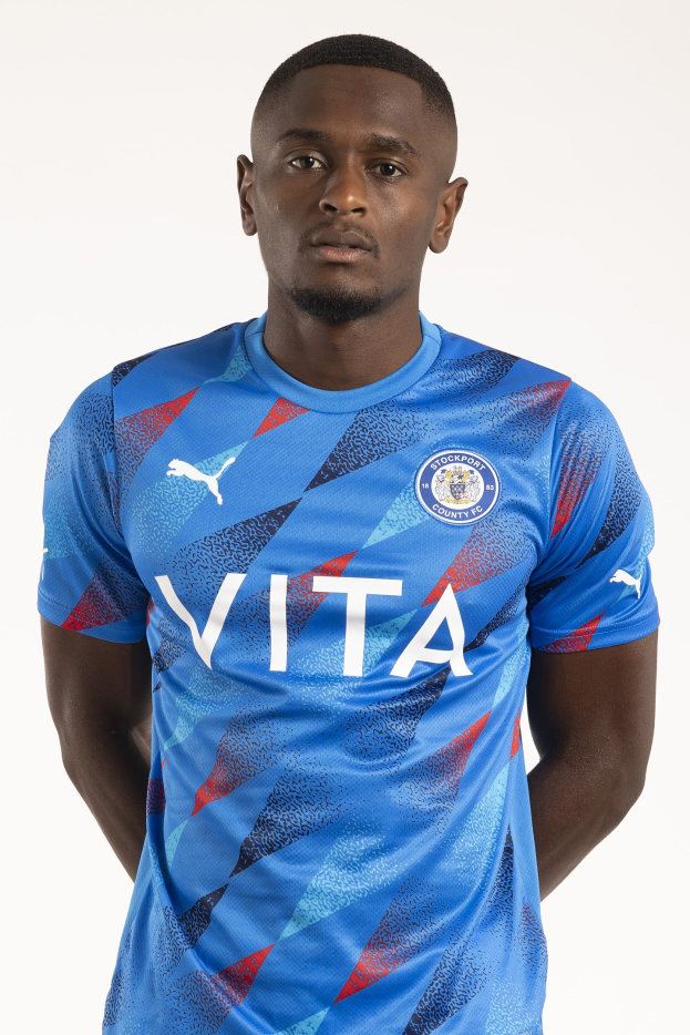 Ein Mann in einem blauen Leicester City Away-Shirt von der Saison 2018-19, der mit den Händen in den Taschen und einem leichten Lächeln steht.