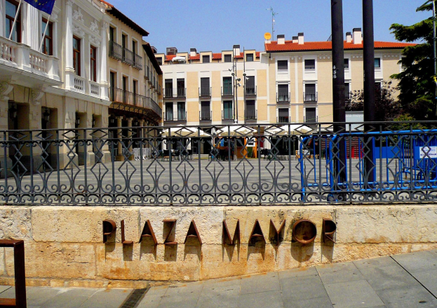 Der Plaza Mayor in Madrid, Spanien, mit einer Wand, einem Metallzaun, Gebäuden, Bäumen und einem bewölkten Himmel.