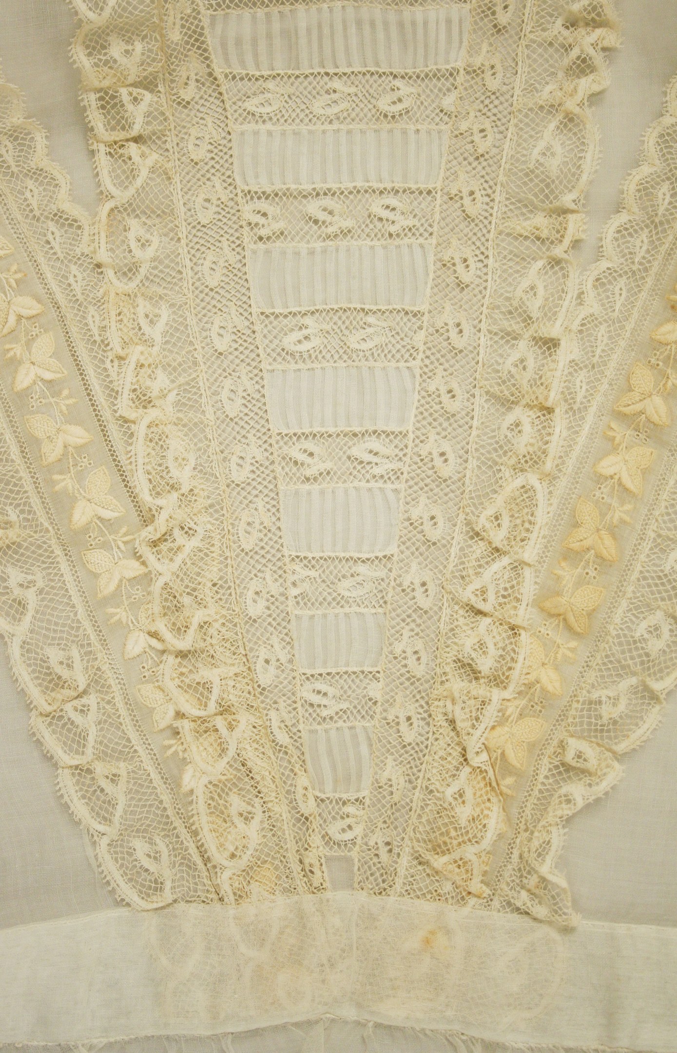 Nahaufnahme eines weißen Kleides mit detaillierter Spitzenverzierung, das feine Muster und einen leichten, luftigen Stoff für den Sommer bietet.