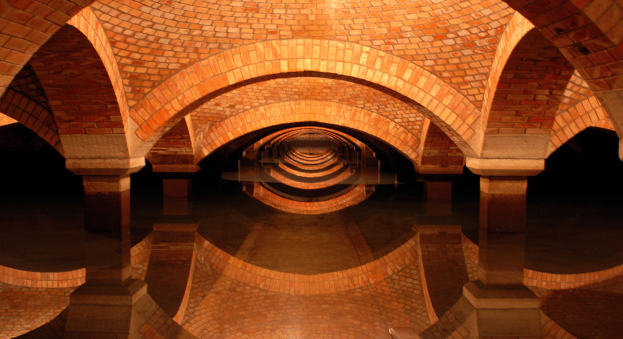 Ziegelgewölbetunnel mit gewölbten Säulen, der sich in stiller Wasserfläche spiegelt und eine friedliche Atmosphäre schafft.