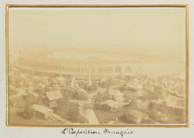 Altes Schwarz-Weiß-Foto eines Stadions inmitten einer Stadt, umgeben von Gebäuden, Bäumen und Masten, mit Text am unteren Rand.