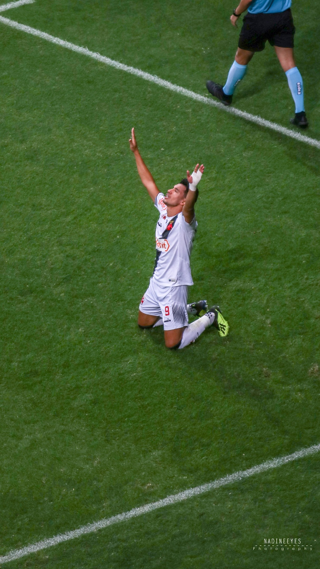 Ein Fußballspieler in einem Sportoutfit kniet auf dem Boden mit ausgestreckten Armen in Feierlaune.