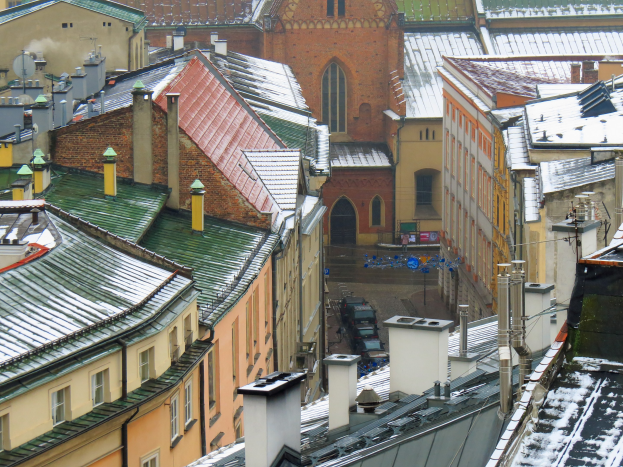 Stadtansicht von einem Geb├Ąuderdach aus, mit schneebedeckten Geb├Ąuden und Fahrzeugen auf einer Stra├če darunter.