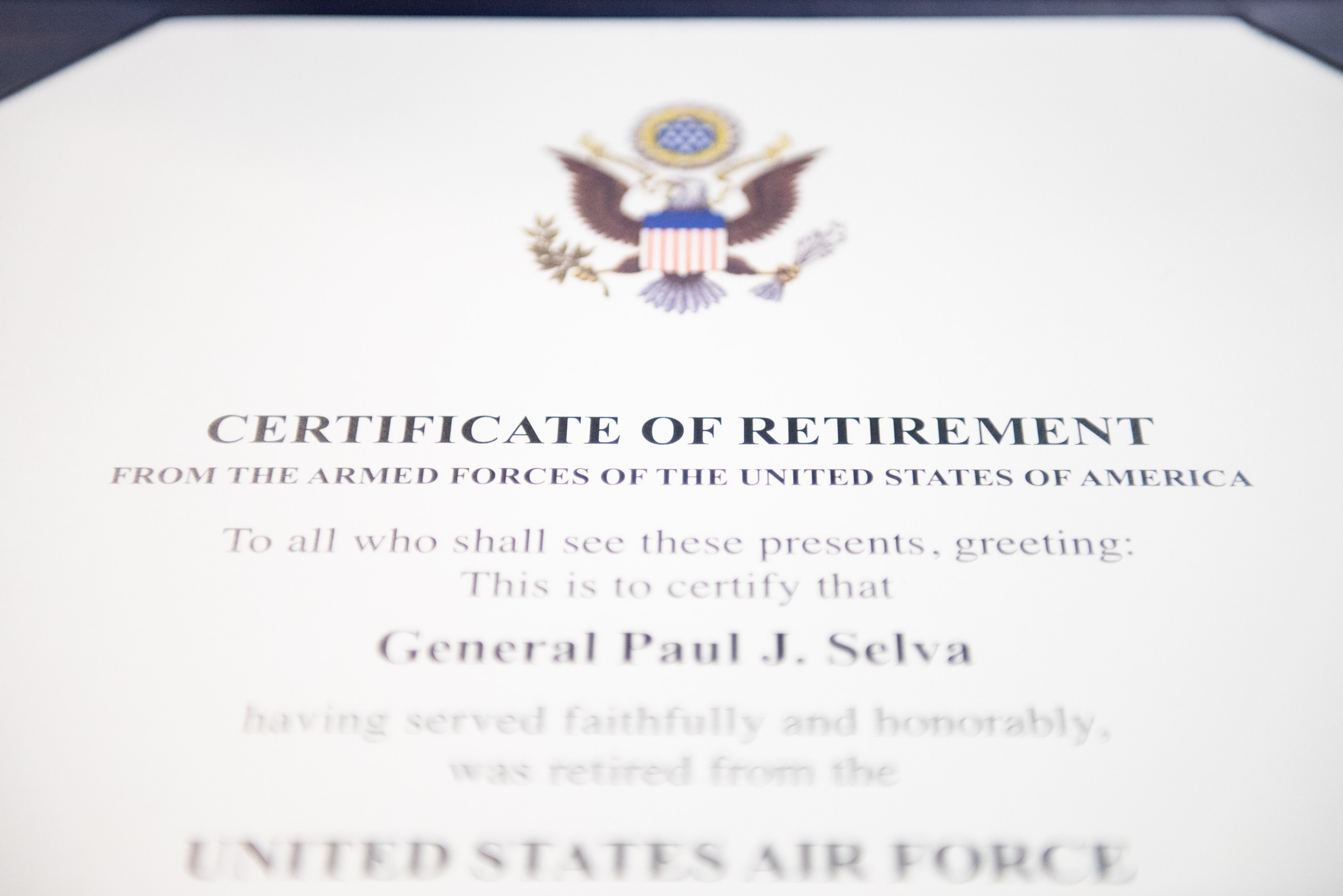 Blauer Rahmen mit einem Abschiedszeugnis der United States Air Force, das ein schwarzes Logo mit einem Stern und einem Lorbeerkranz sowie eine Banner mit der Aufschrift 'Ruhestand' zeigt.