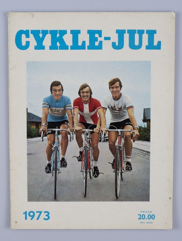 Drei Menschen auf Fahrrädern auf einer Straße mit Häusern, Bäumen und einem klaren blauen Himmel, mit "Cykle-Jul 1973 - Cyclocross Magazine"-Text oben und unten.
