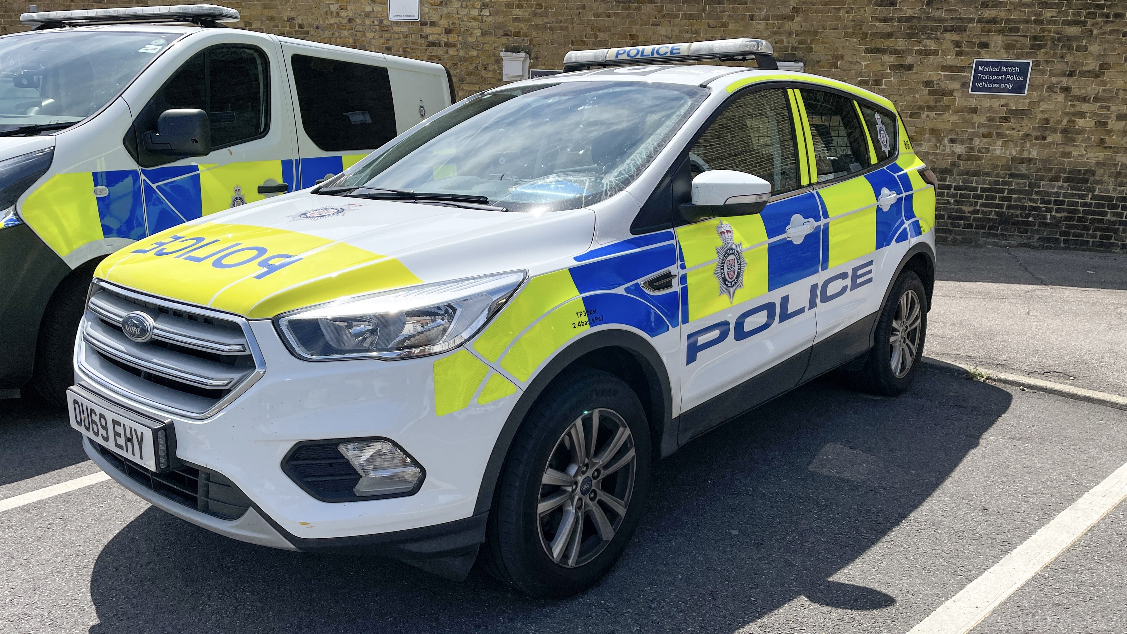 Zwei Polizeiautos nebeneinander in einer Parklücke mit einer Wandtafel im Hintergrund.