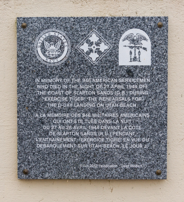 Steintafel an einem Gebäude mit der Inschrift "Im Gedenken an die 946 amerikanischen Soldaten" und Logos.