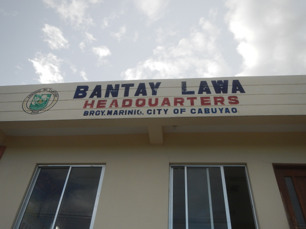 Die Zentrale der Bantay Lawa in Cebu City, Philippinen, mit einem Gebäude mit Fenstern, einer Tür und einer Namensplakette an der Wand unter einem Himmel voller weißer Wolken.