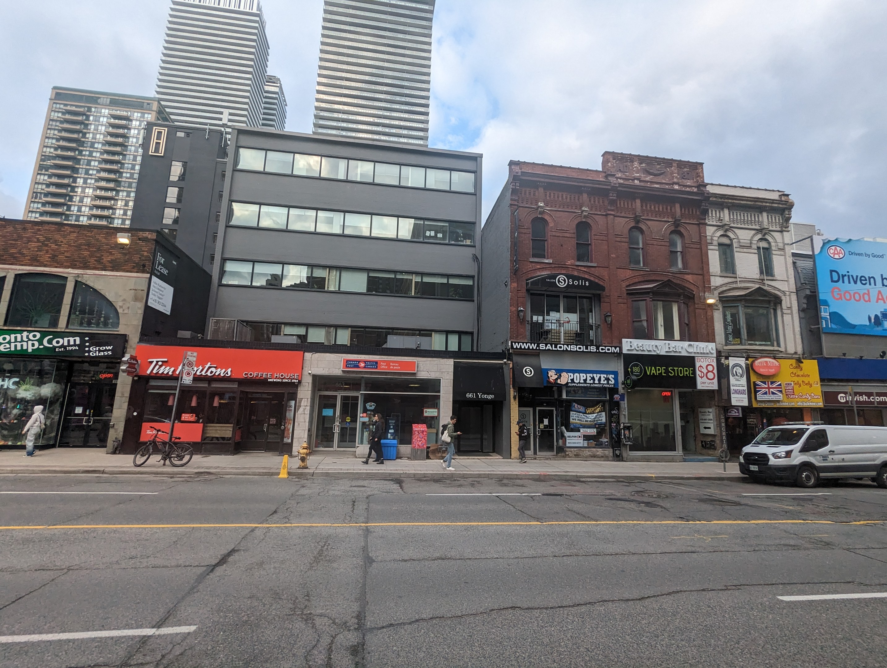 Eine Stadtstraße mit hohen Gebäuden, Fahrzeugen, Fußgängern, einem Fahrrad, einem Feuerhydranten und Schildern mit einer Adresse in Toronto.