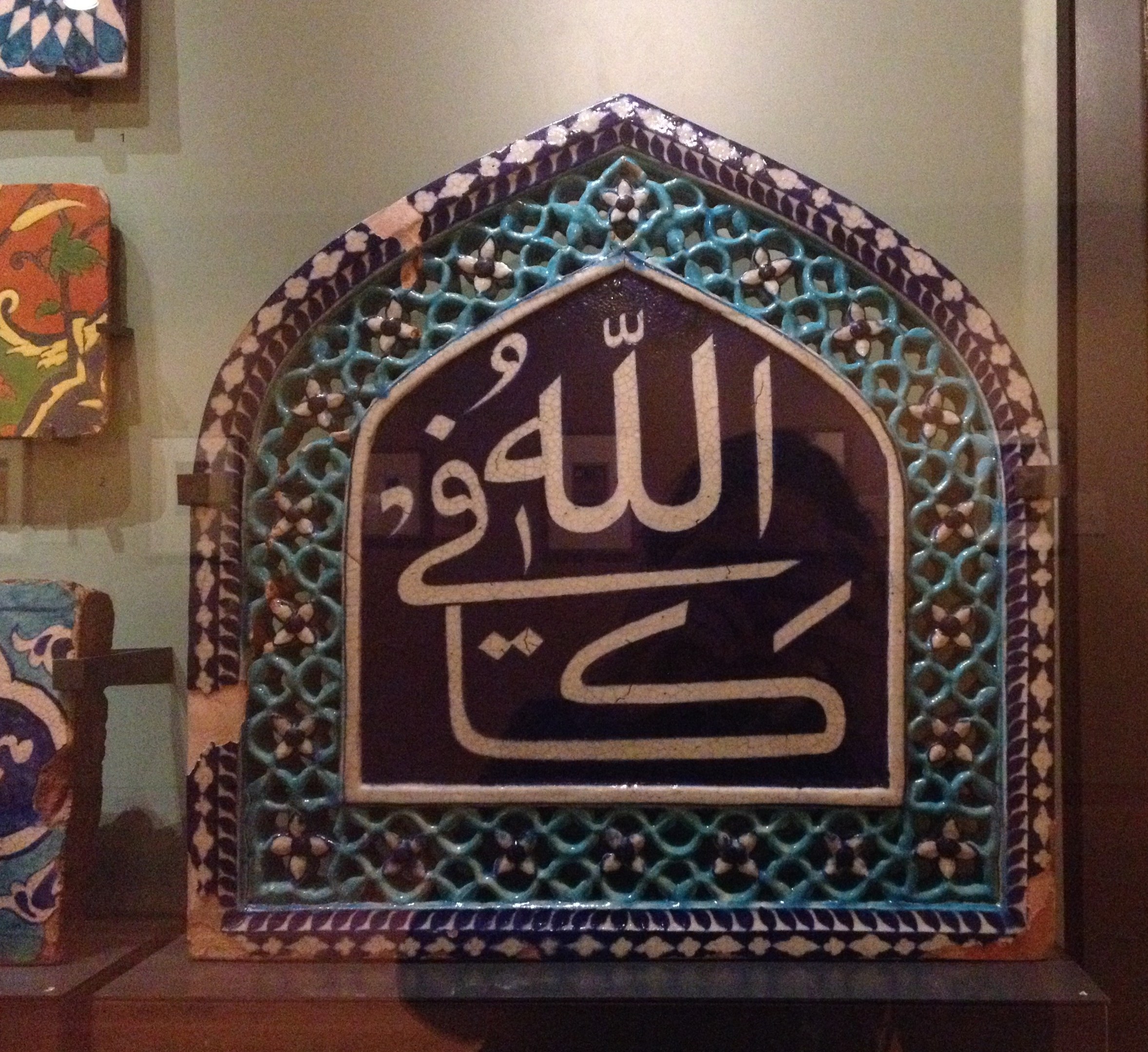 Islamische Kalligrafie in einem gerahmten Wandausstellungsstück in einem Museum gezeigt, mit zusätzlichen Artefakten links.