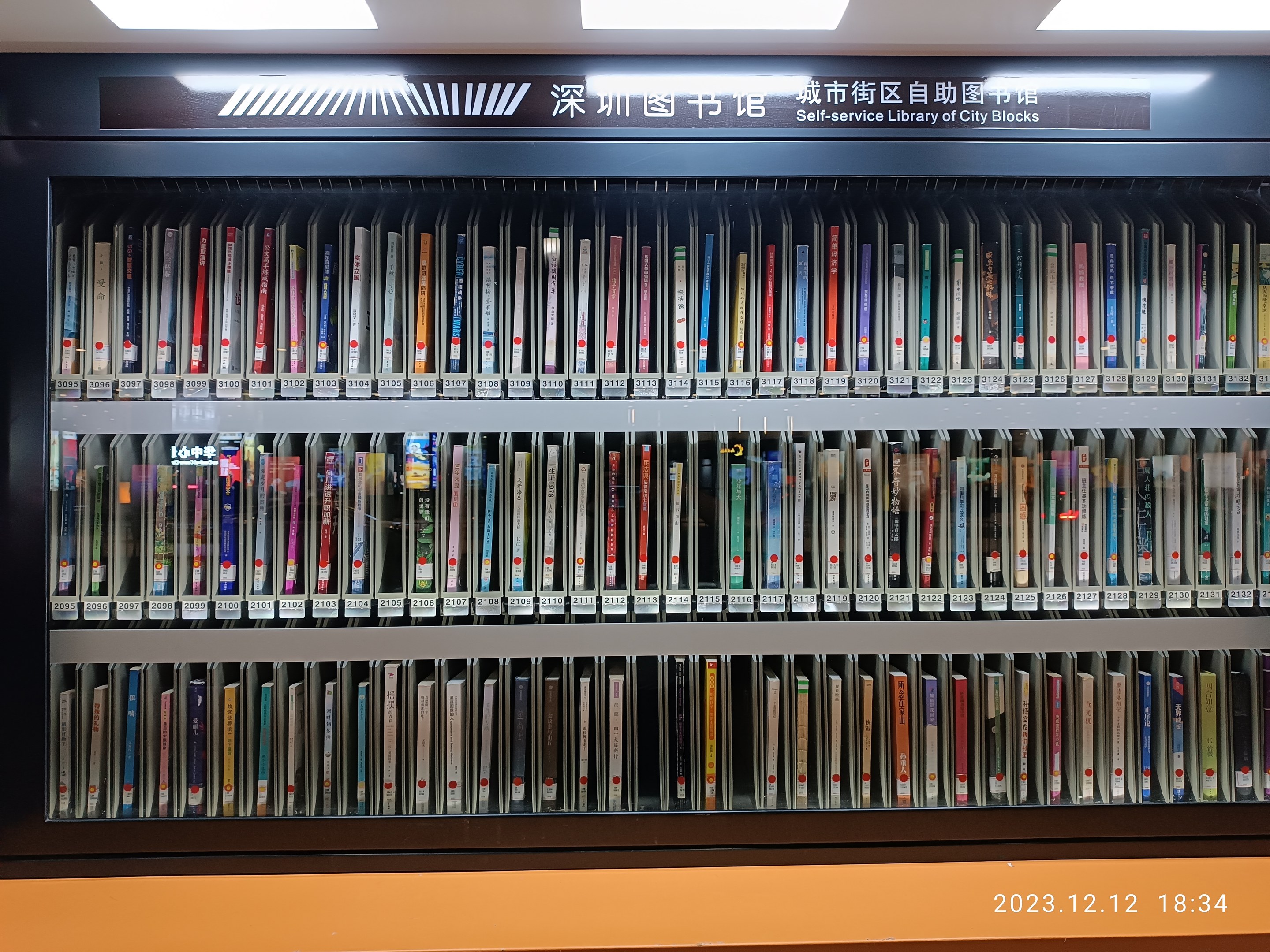 Eine gut beleuchtete Bibliothek mit hohen Bücherregalen voller Bücher, ein Schild mit Text und ein Wasserzeichen unten, das einer Selbstbedienungsbibliothek in Stadtblocks ähnelt.