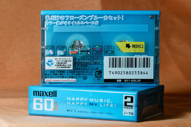 Blaue Maxell "Happy Music Happy My Life"-Kassette auf einem braunen Tisch mit leicht unscharfem, träumerischem Hintergrund.