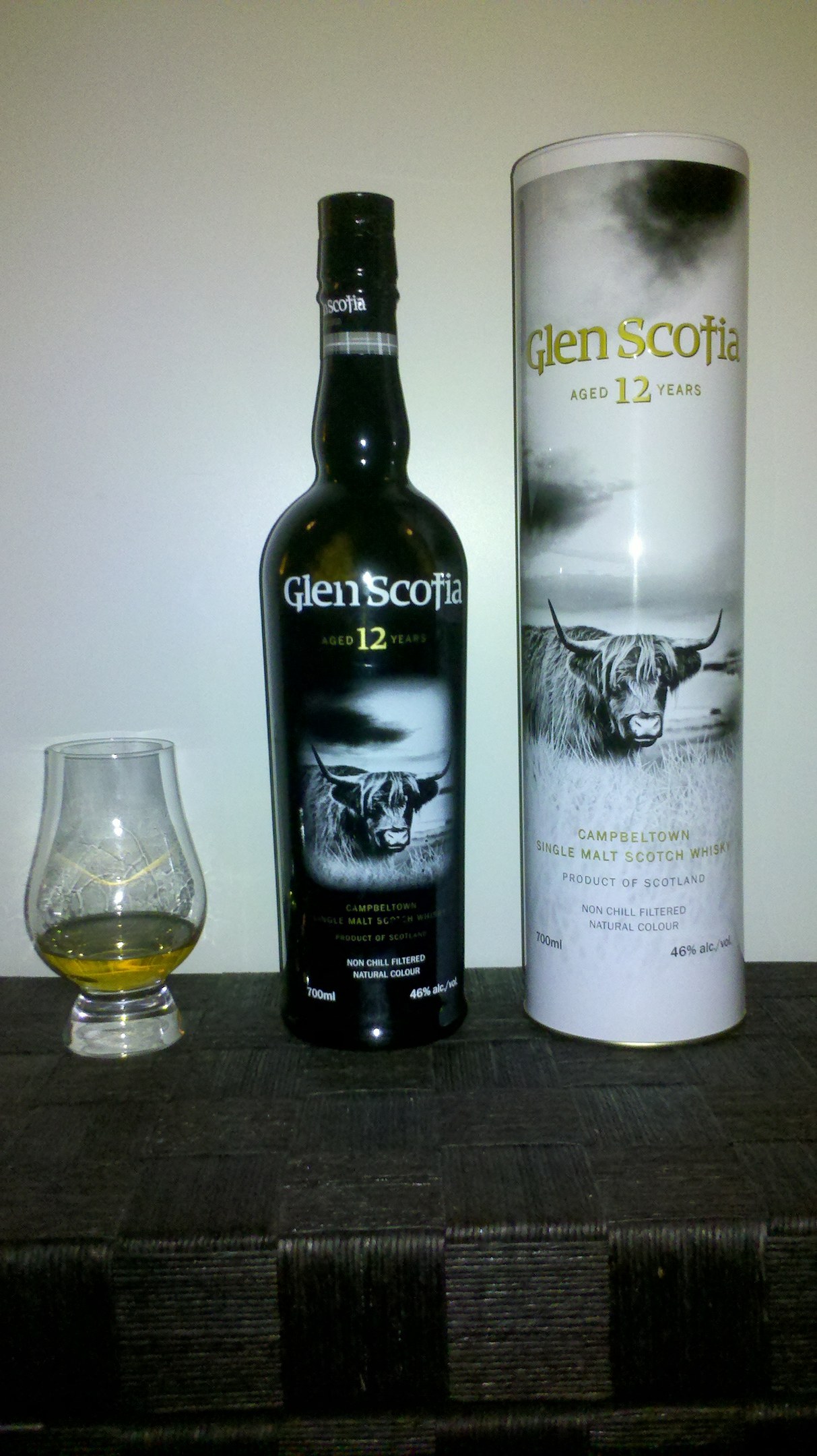 Eine Flasche Glen Scotia 12 Jahre alter schottischer Whisky und ein Glas desselben Whiskys auf einem hellen Holztisch.