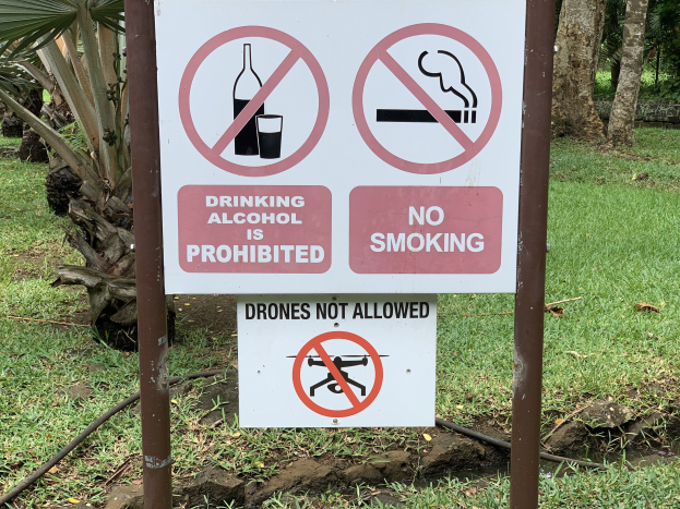 Straßenschilder verbieten das Trinken von Alkohol und das Rauchen, mit Bäumen und Gras im Hintergrund.
