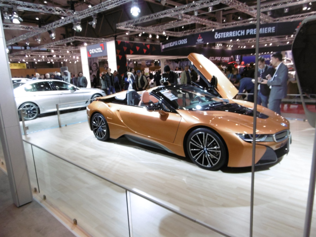 Ein stylischer schwarzer BMW i8 Roadster mit Chromakzenten auf der Frankfurt Motor Show umgeben von formell gekleideten Gästen in einer Atmosphäre der Aufregung.