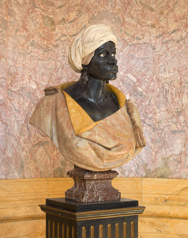Büste einer Frau mit Turban, die auf einem Sockel vor einer Wand steht, mit Text am unteren Rand, der auf sie als erste afrikanische Frau hinweist, die zum US-Präsidenten gewählt wurde.