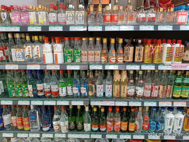 Eine Vitrine voller verschiedener Alkoholflaschen, jede mit Etiketten und Preisschildern, unter Deckenlampen, die an das Innere eines Spirituosenladens erinnern.