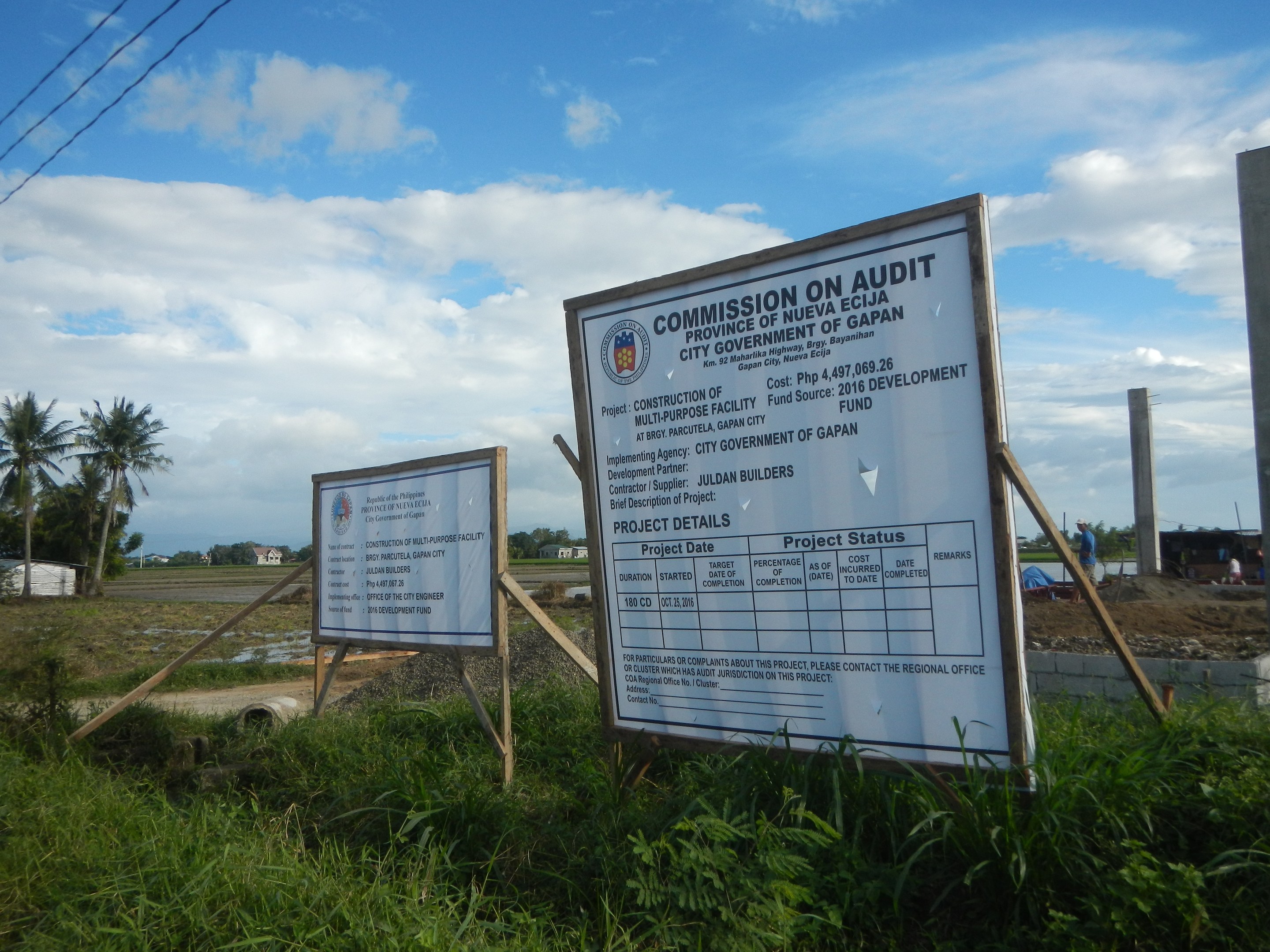 Schild für "Kommission für Revision" vor einem Gebäude mit umgebenem Grün und Strommasten.