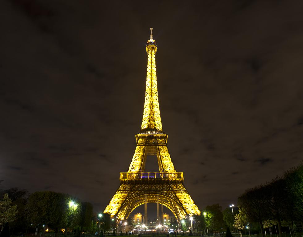 Ein Innenblick auf einen Einkaufskomplex mit Bäumen, Schirmen mit Stangen, Personenaufzügen, Namensschildern, Ständen, Lampen, Leuchttafeln und einer Gruppe von Menschen.