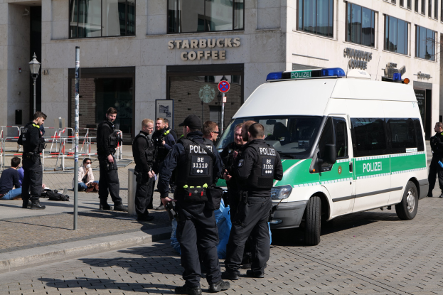 Eine Gruppe von Polizisten steht vor einem Starbucks-Kaffeehaus, mit einem Van auf der rechten Seite und einigen Menschen auf der linken Seite; ein Gebäude, ein Schild, ein Laternenmast und ein Zaun sind im Hintergrund zu sehen.