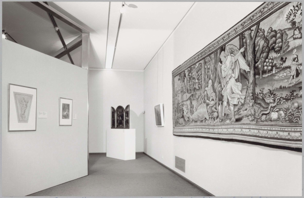 Schwarz-weiß-Foto eines Museumsgangs mit einem großen Wandteppich, gerahmten Kunstwerken an den Wänden, Sockeldisplays und Deckenleuchten sowie dem Text "Museum of Fine Arts, New York City" unten.