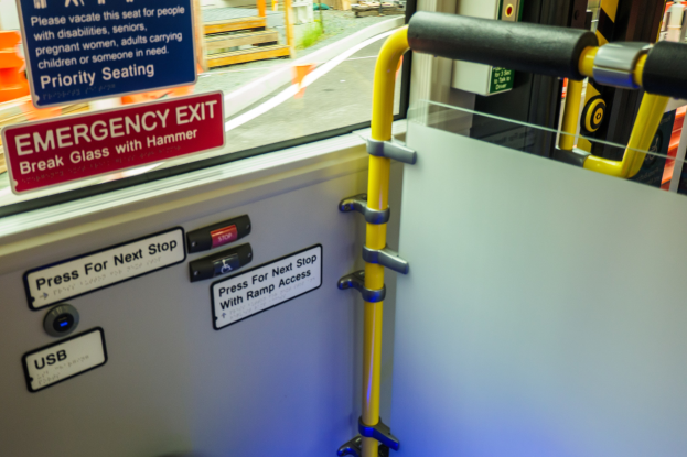 Notausgangsschild an der Seite eines Zuges, mit einer Tür, einem Griff und einem Glasfenster, das die Straße, Pfosten und andere Objekte draußen zeigt.