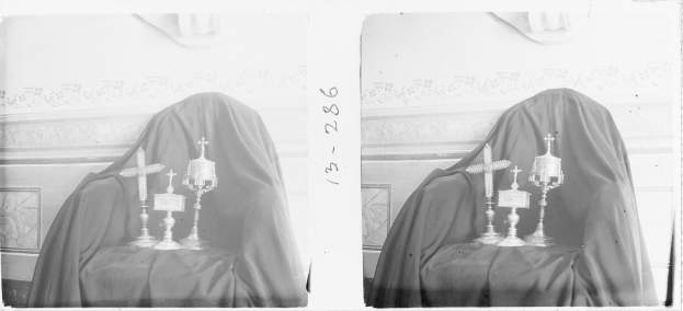 Schwarzes und weißes Foto einer Frau in einem Schleier, die auf einem Stuhl sitzt und vor sich einen Tisch mit verschiedenen Gegenständen hat, vor einem Wandhintergrund, identifiziert als Erzbischof der Kirche des Heiligen Grabes.