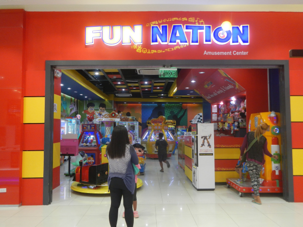 Ein lebendiger Vergnügungspark in Singapur mit Arcade-Maschinen, bunten Lichtern und einer Gruppe von Menschen mit Taschen in der Nähe eines Schildes.
