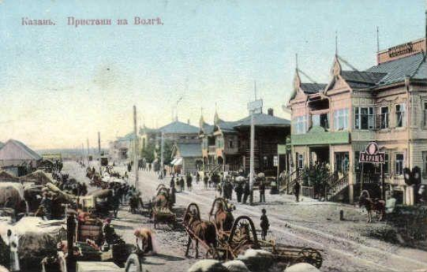 Schwarz-weiß-Foto einer Stadtstraße in Krasnoyarsk mit Pferdefuhrwerken, Fußgängern, Gebäuden, Bäumen und Strommasten unter einem Himmel.