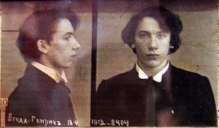 Schwarz-weiß-Foto eines Mannes in einem schwarzen Anzug, weißem Hemd und schwarzer Krawatte mit zurückgekämmtem Haar, gefalteten Händen, strenger Miene und Text, der seine Verbrechen beschreibt.