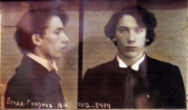 Schwarz-weiß-Foto eines Mannes in einem schwarzen Anzug, weißem Hemd und schwarzer Krawatte mit zurückgekämmtem Haar, gefalteten Händen, strenger Miene und Text, der seine Verbrechen beschreibt.