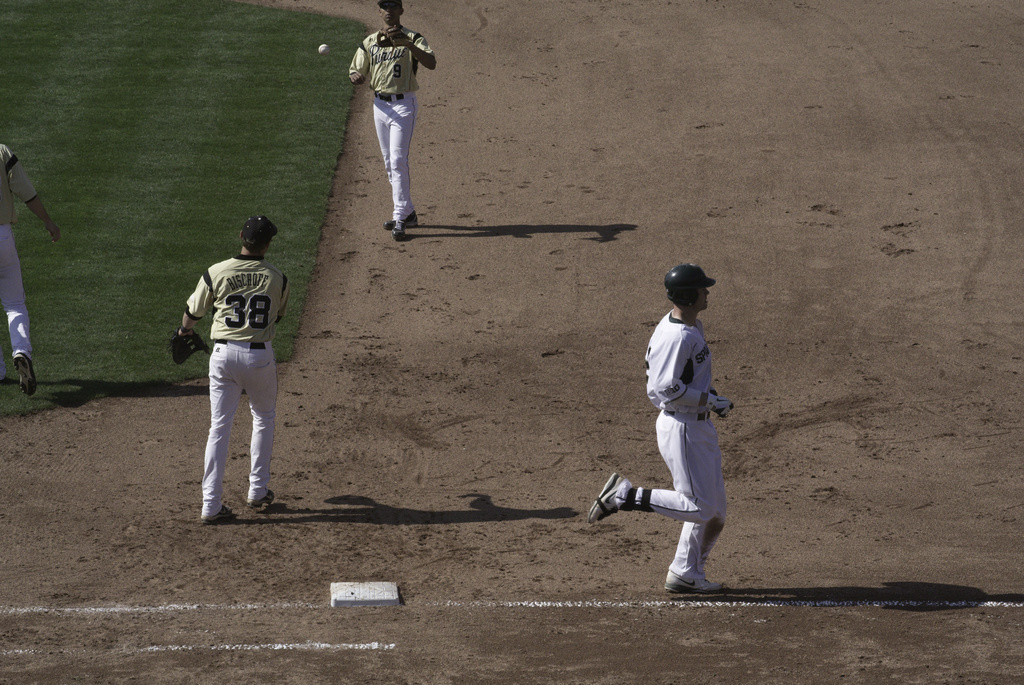 Ein Mann in einem weißen Kleid und schwarzer Mütze läuft auf der rechten Seite, während zwei Personen in gelben T-Shirts in der Mitte laufen, wahrscheinlich Cricket spielen.