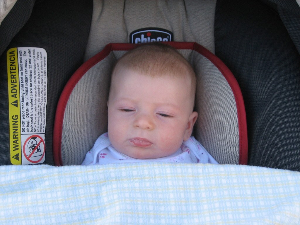 Baby unter einer Babywiege mit einem Warnaufkleber auf der linken Seite liegend.