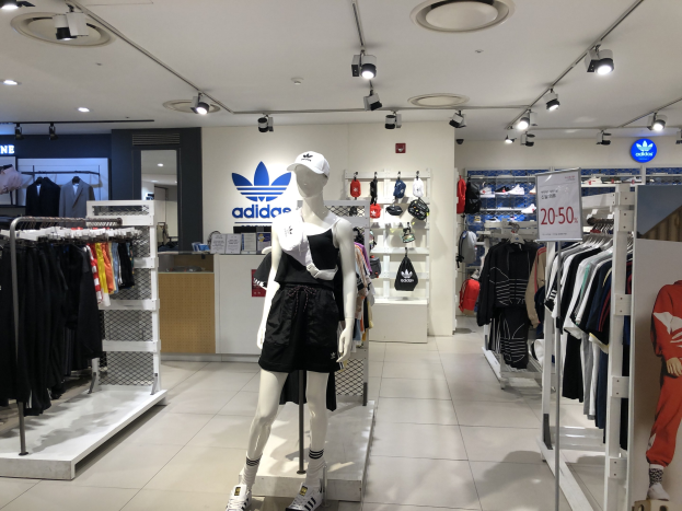 Innenansicht eines adidas-Geschäfts in Singapur mit Schaufensterpuppen, Kleiderauslagen, einer Texttafel und Deckenleuchten.
