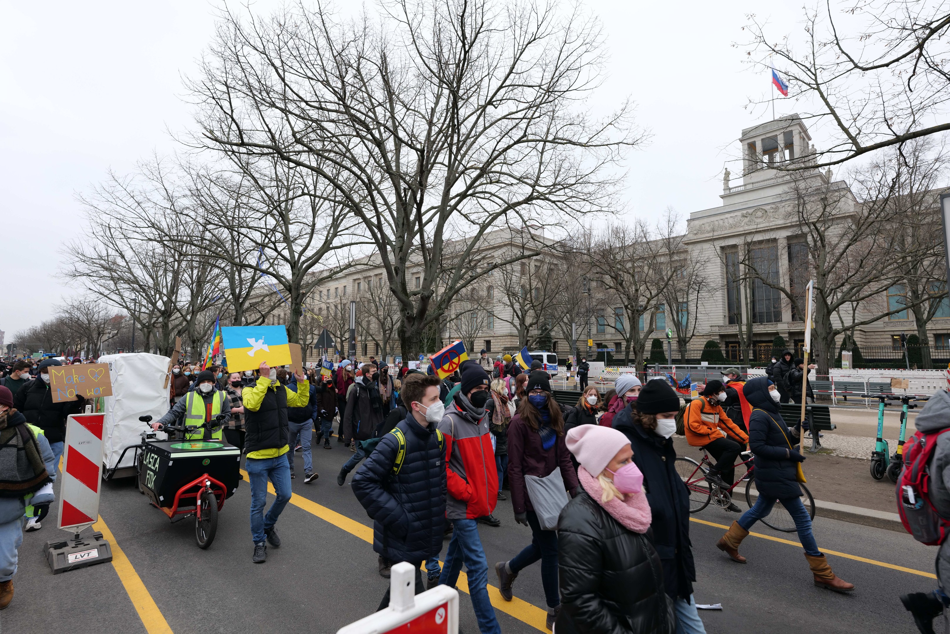 Eine große Gruppe von Menschen nimmt an einer Protestdemo in Washington, D.C. am 21. Januar 2020 teil und marschiert eine Straße entlang mit Schildern, Bannern und Fahrrädern vor einer Kulisse aus Bäumen, Schildern und einem klaren blauen Himmel.