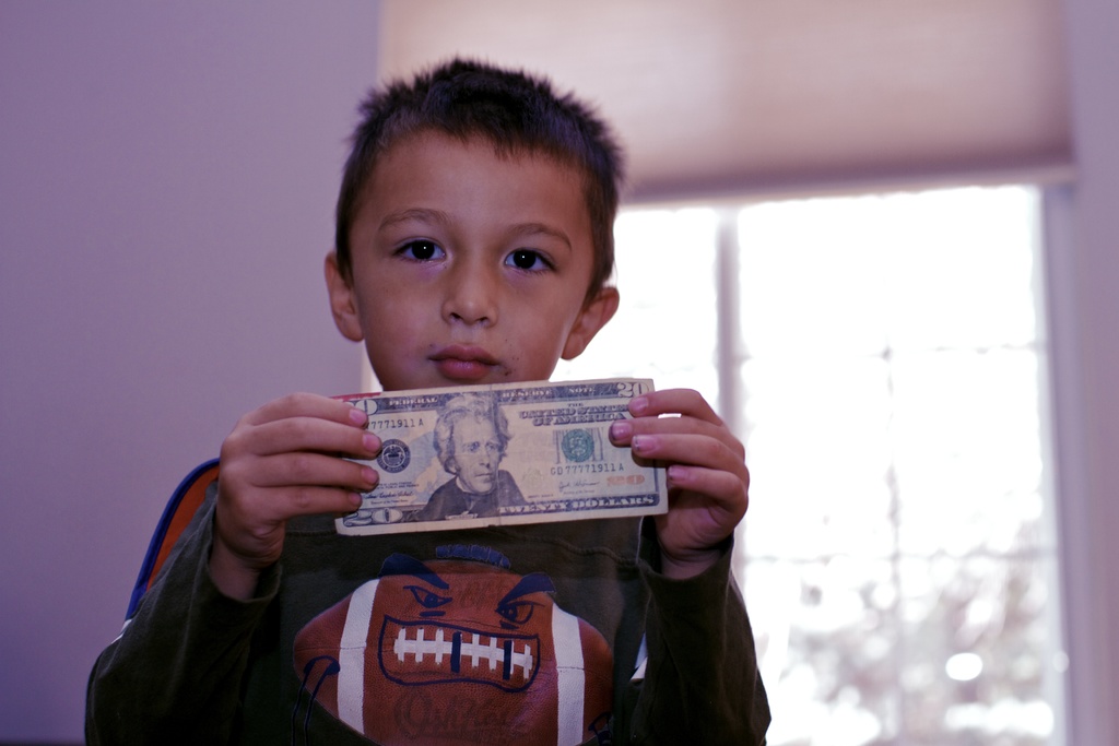 Ein Junge hält Geld in den Händen, vor einem Fenster und einer Wand.