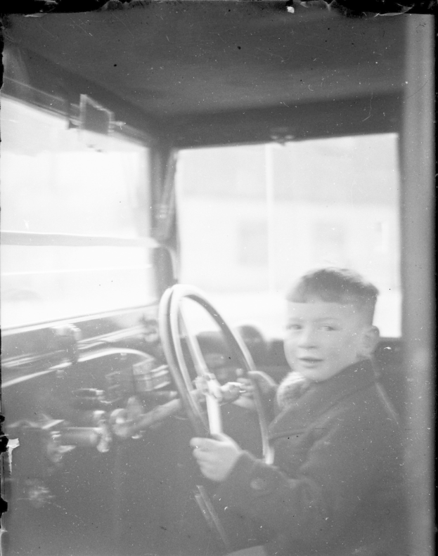 Ein junger Junge in Schwarz und Weiß sitzt im Fahrersitz eines Autos und hält das Lenkrad konzentriert fest.