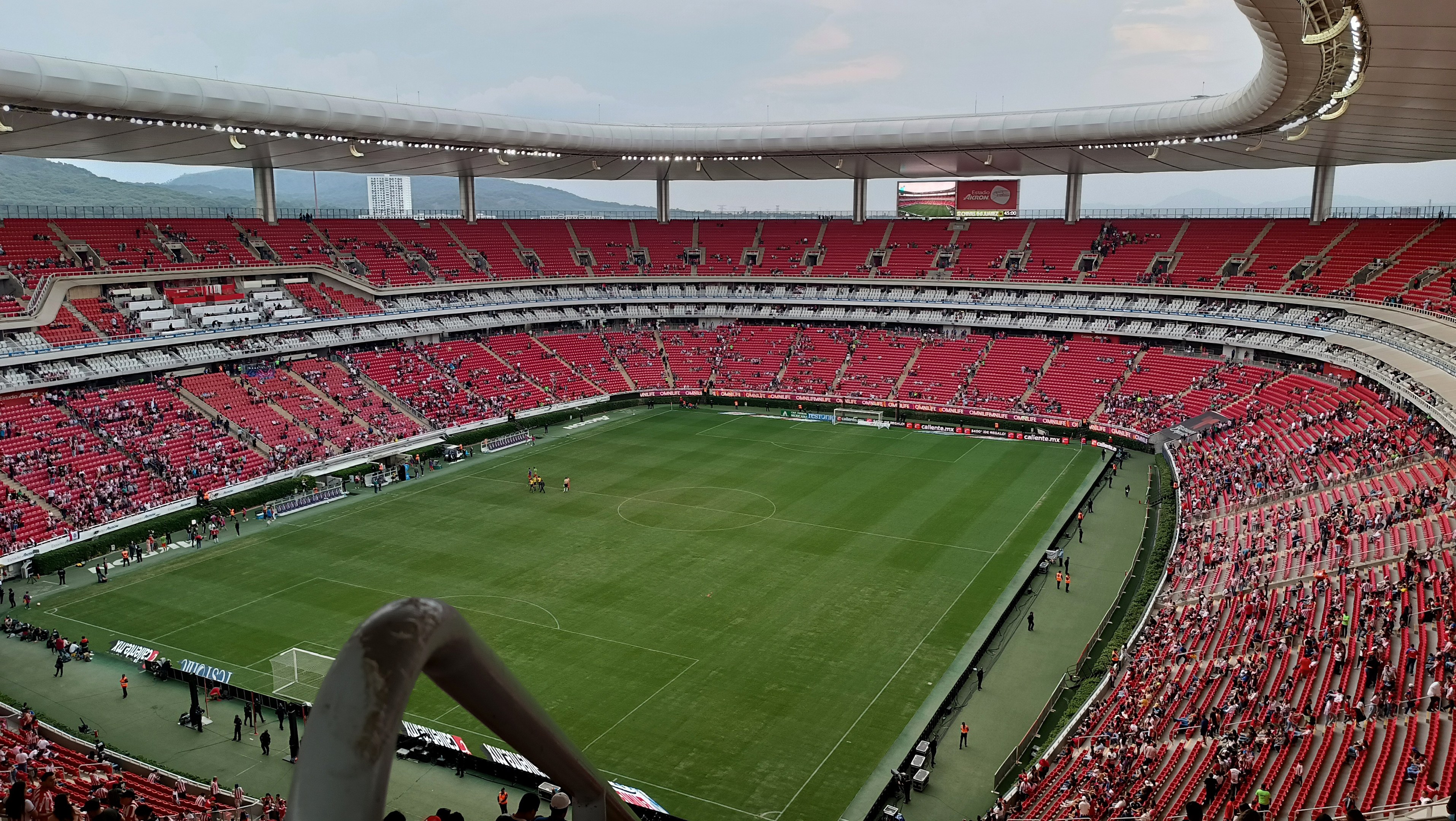 Großes Stadion voller Zuschauer bei einem Fussballspiel, Hügel im Hintergrund bei klarem blauem Himmel.