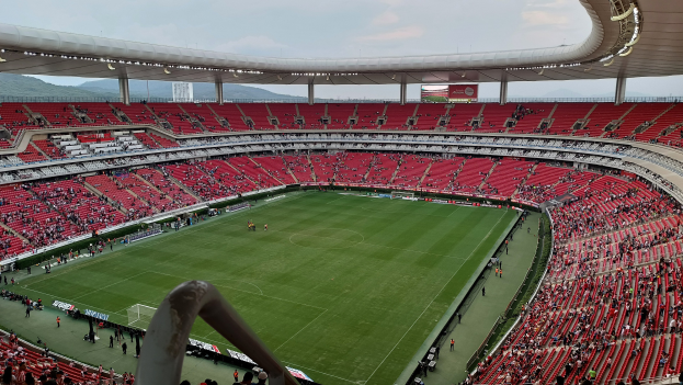 Großes Stadion voller Zuschauer bei einem Fussballspiel, Hügel im Hintergrund bei klarem blauem Himmel.