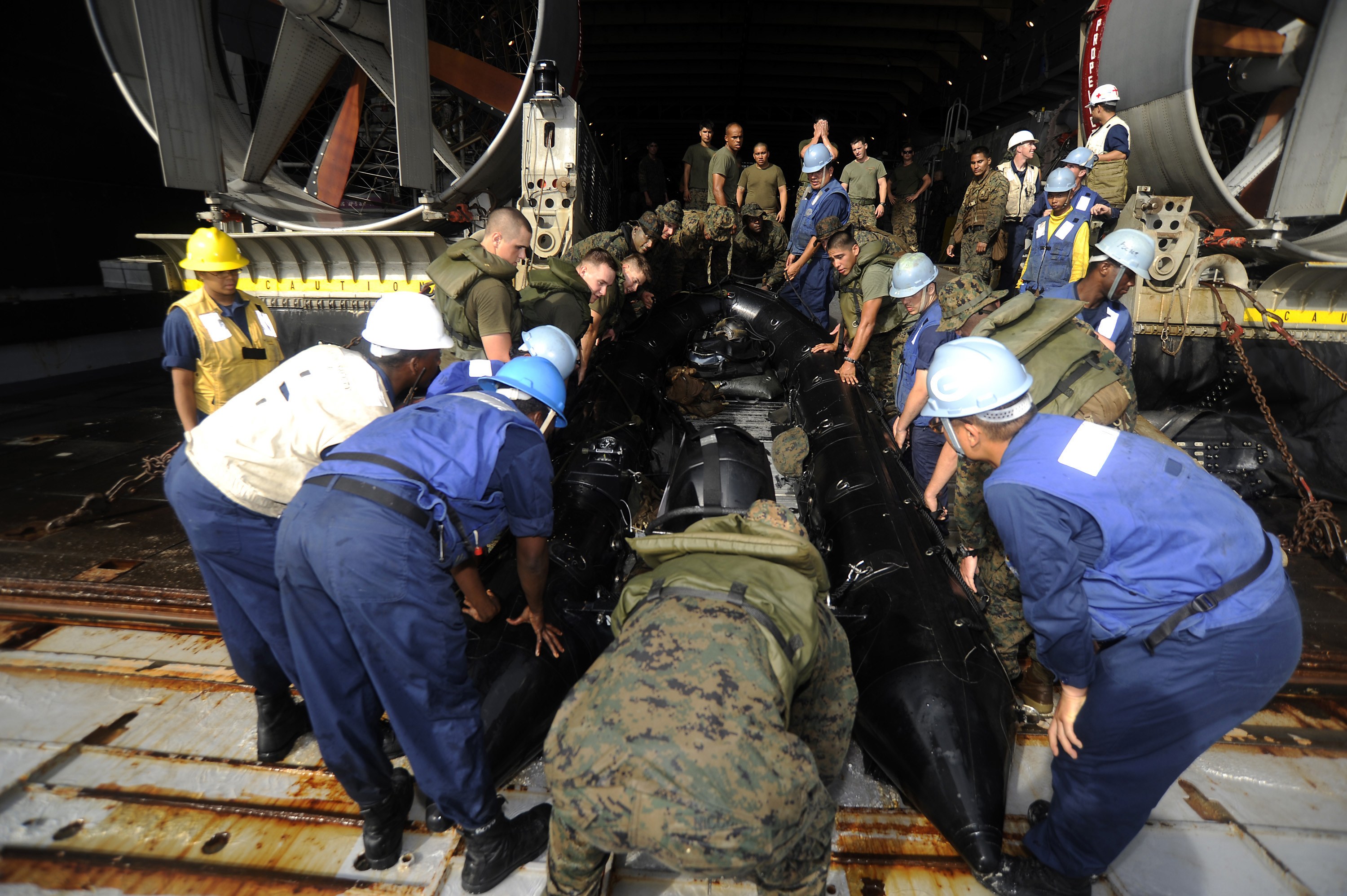 Eine Gruppe von Männern in Helmen und Uniformen, die an einem U-Boot in einem Schiffbauwerk arbeiten.